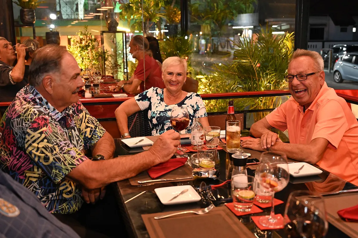 Três amigos sorrindo e brindando durante um jantar em restaurante