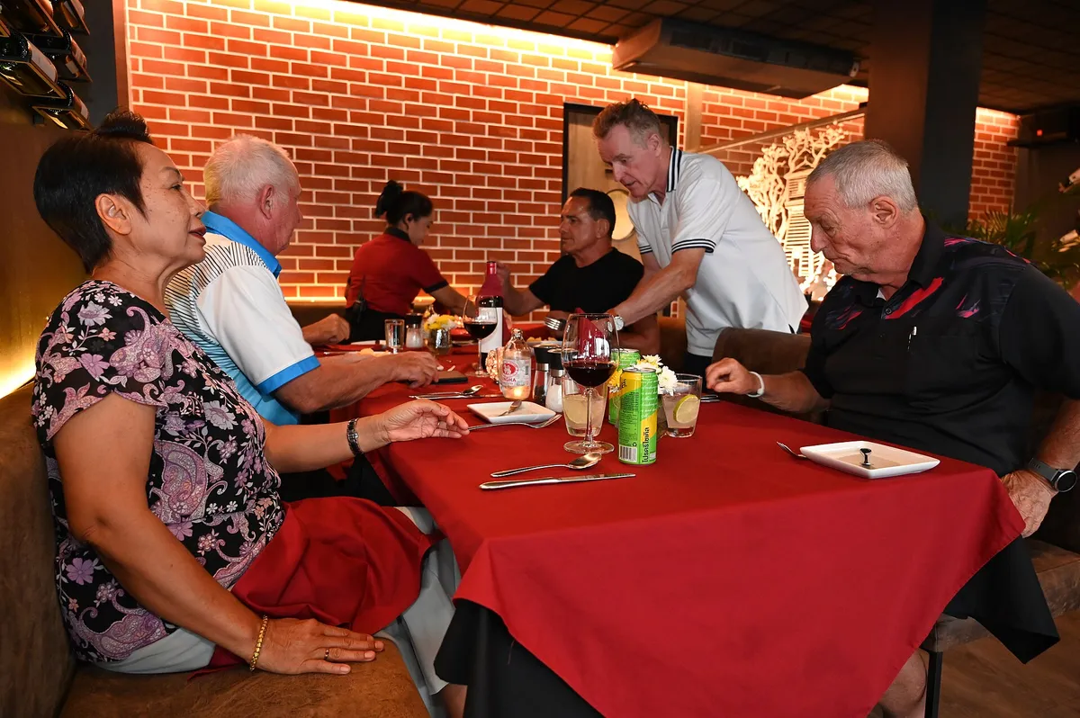 Grupo de amigos conversando e rindo em volta de uma mesa de restaurante com taças de vinho