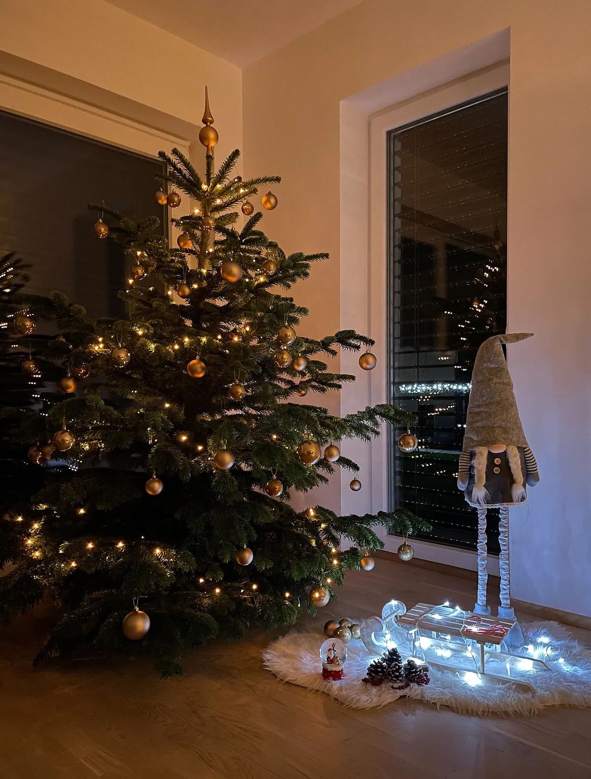 Árvore de Natal decorada com bolas douradas e luzes acesas em uma sala, à noite