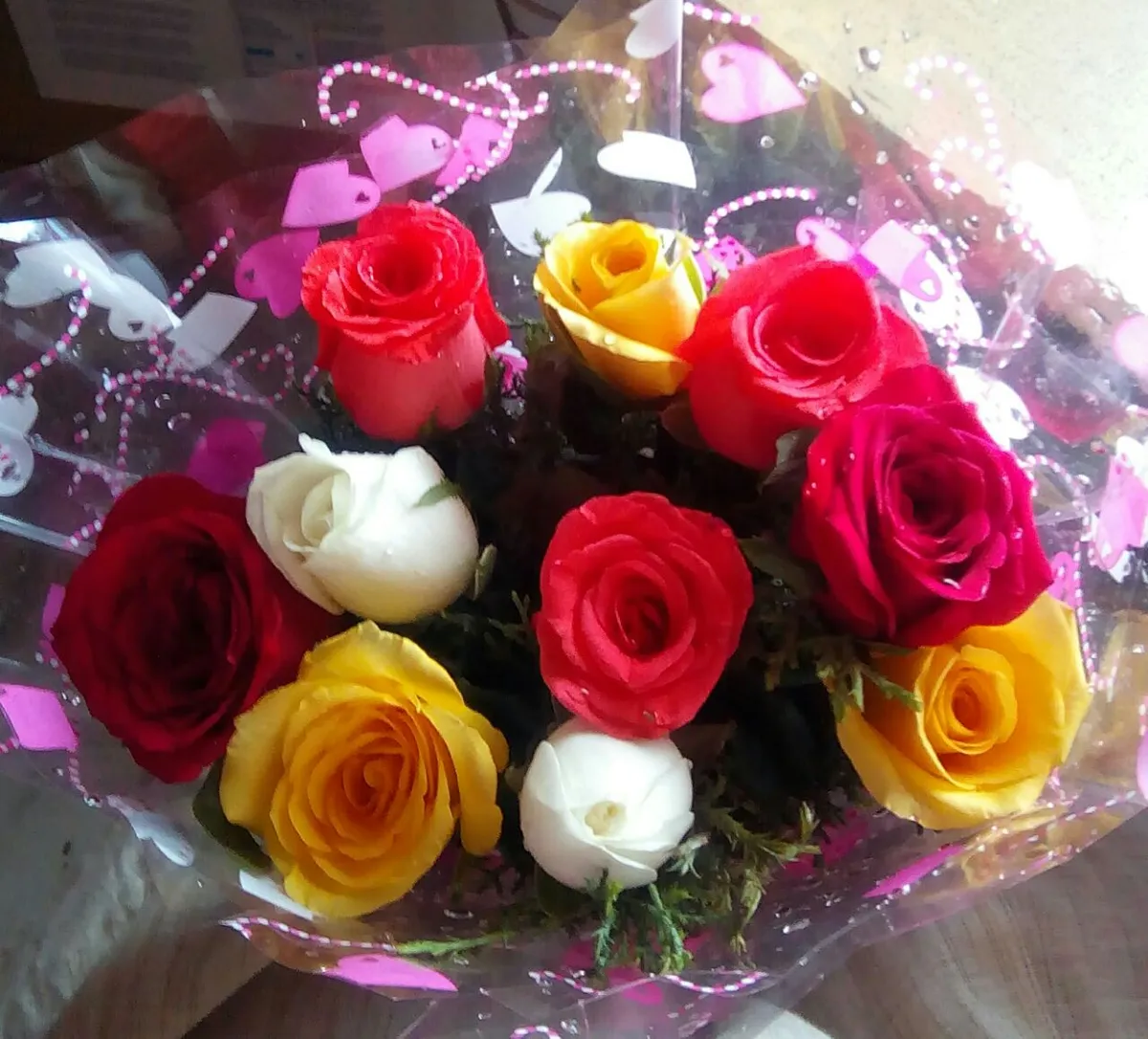 Buquê de rosas vermelhas, amarelas e brancas embrulhado em papel transparente com corações