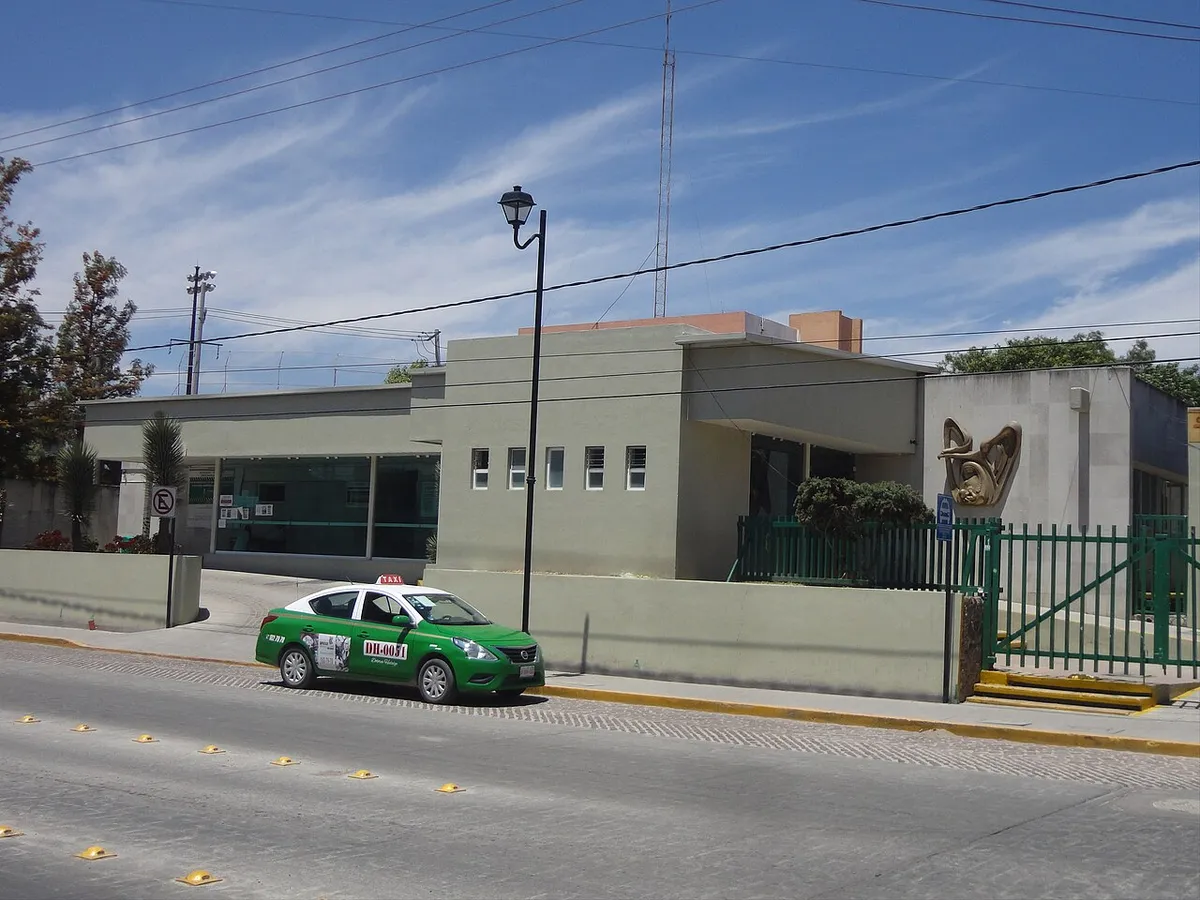 Fachada de una clínica de primer nivel vista desde la calle, con su acceso y un taxi verde estacionado