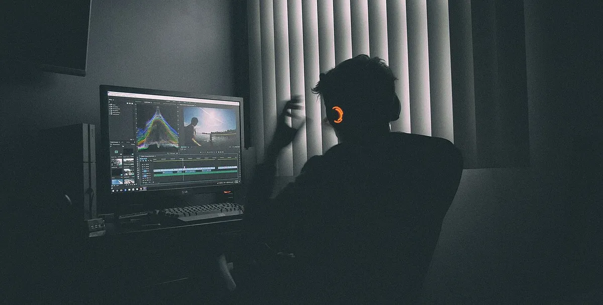 Persona trabajando frente a su computadora en una habitación con poca luz