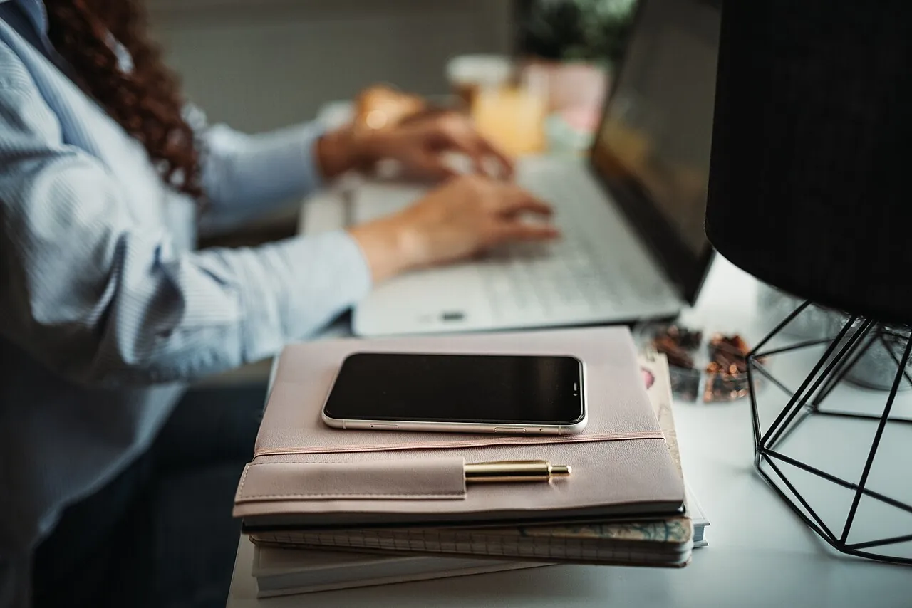 Persona trabajando en una laptop con su agenda y su celular sobre el escritorio
