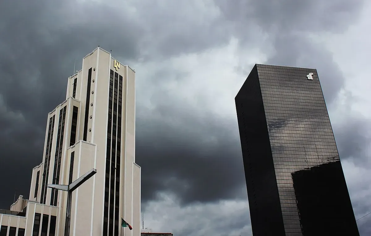 Edificio de la Lotería Nacional junto a una torre oscura, con cielo nublado