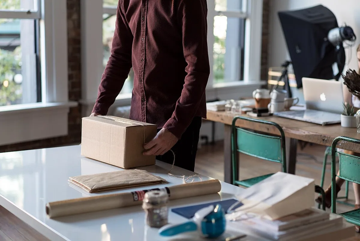 A person packing belongings into a cardboard box on an office desk
