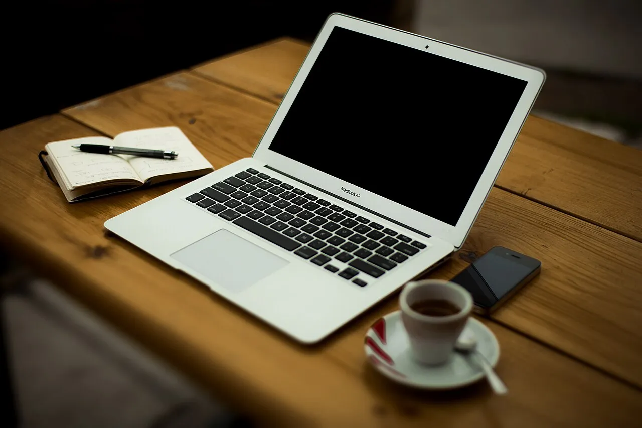 Escritorio en casa con una computadora portátil abierta, una libreta con bolígrafo y un teléfono
