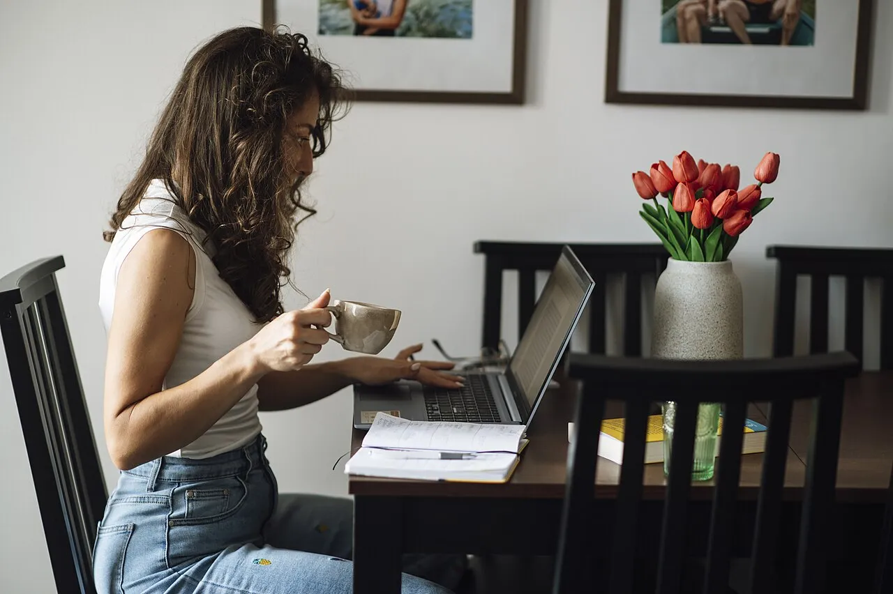 Mujer estudiando en casa con una computadora portátil, una libreta y una taza sobre la mesa