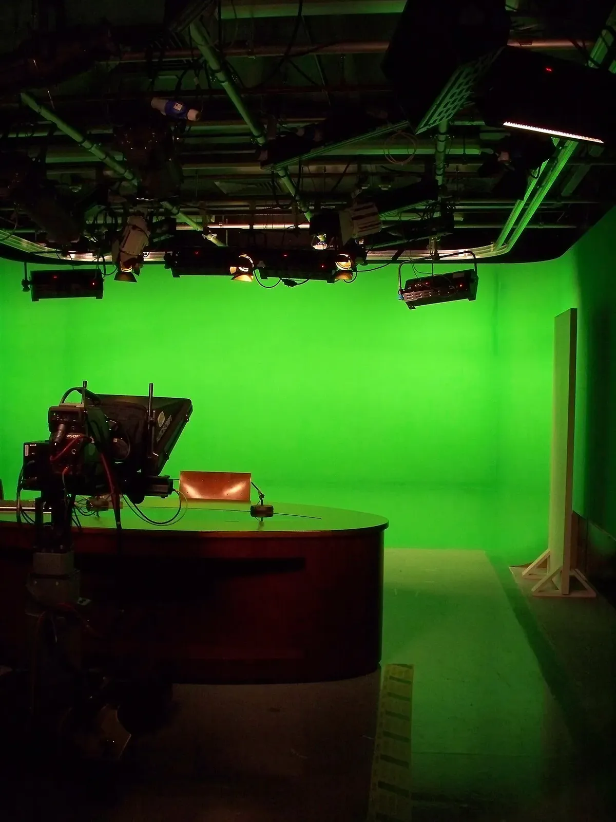 Estudio de televisión con cámara, mesa de presentador y fondo verde