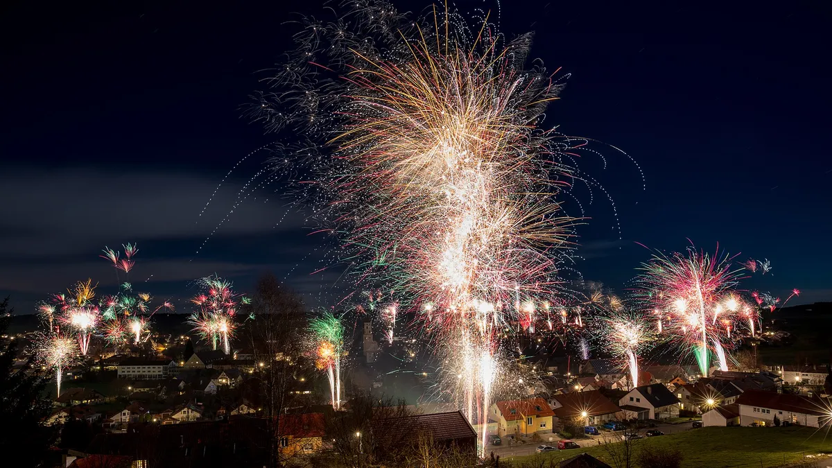 Fogos de artifício coloridos explodindo no céu noturno sobre uma vila na virada do ano