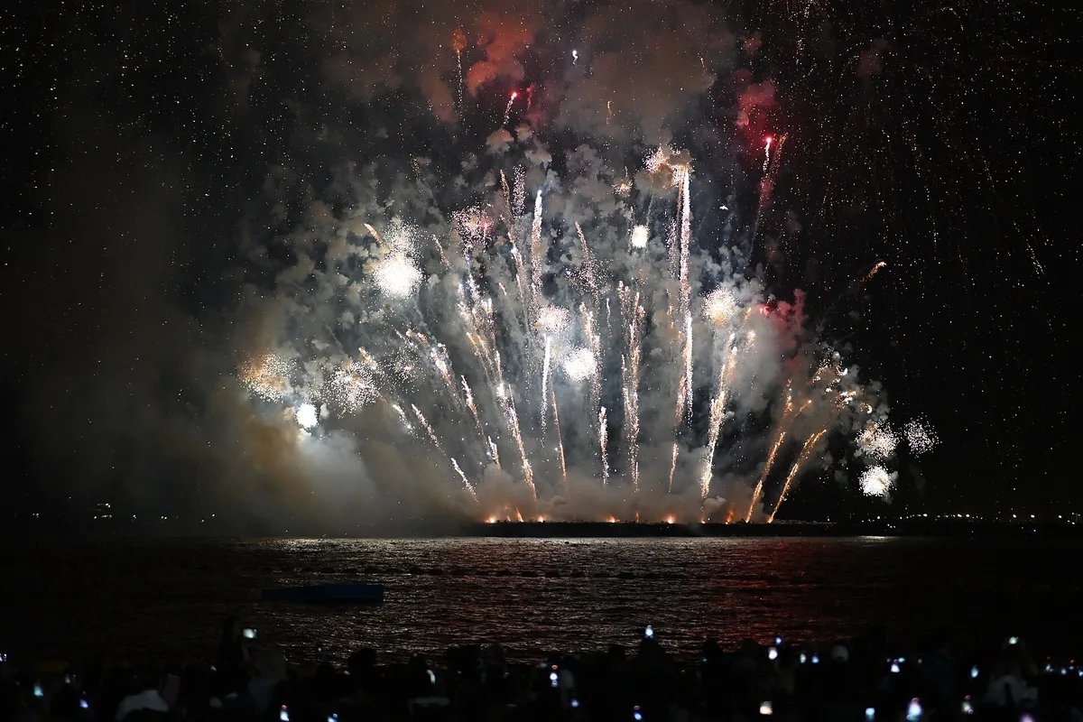 Show de fogos de artifício sobre o mar assistido por uma multidão na praia, na noite de Réveillon