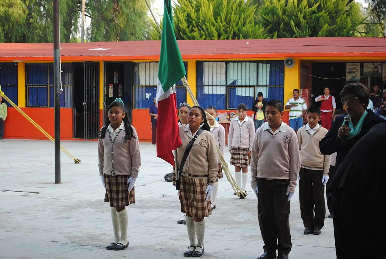 Escolta de estudiantes uniformados rindiendo honores a la Bandera en el patio de una secundaria