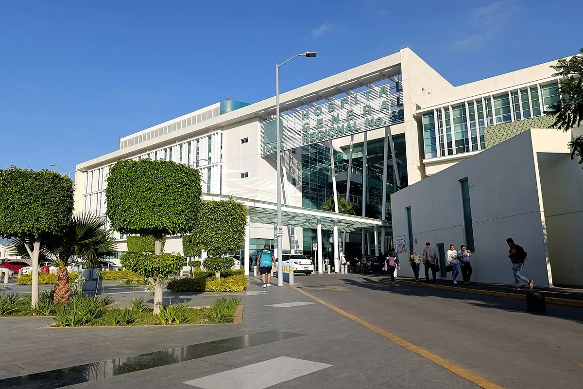 Fachada de un hospital público moderno con cristalera y acceso techado para ambulancias y pacientes