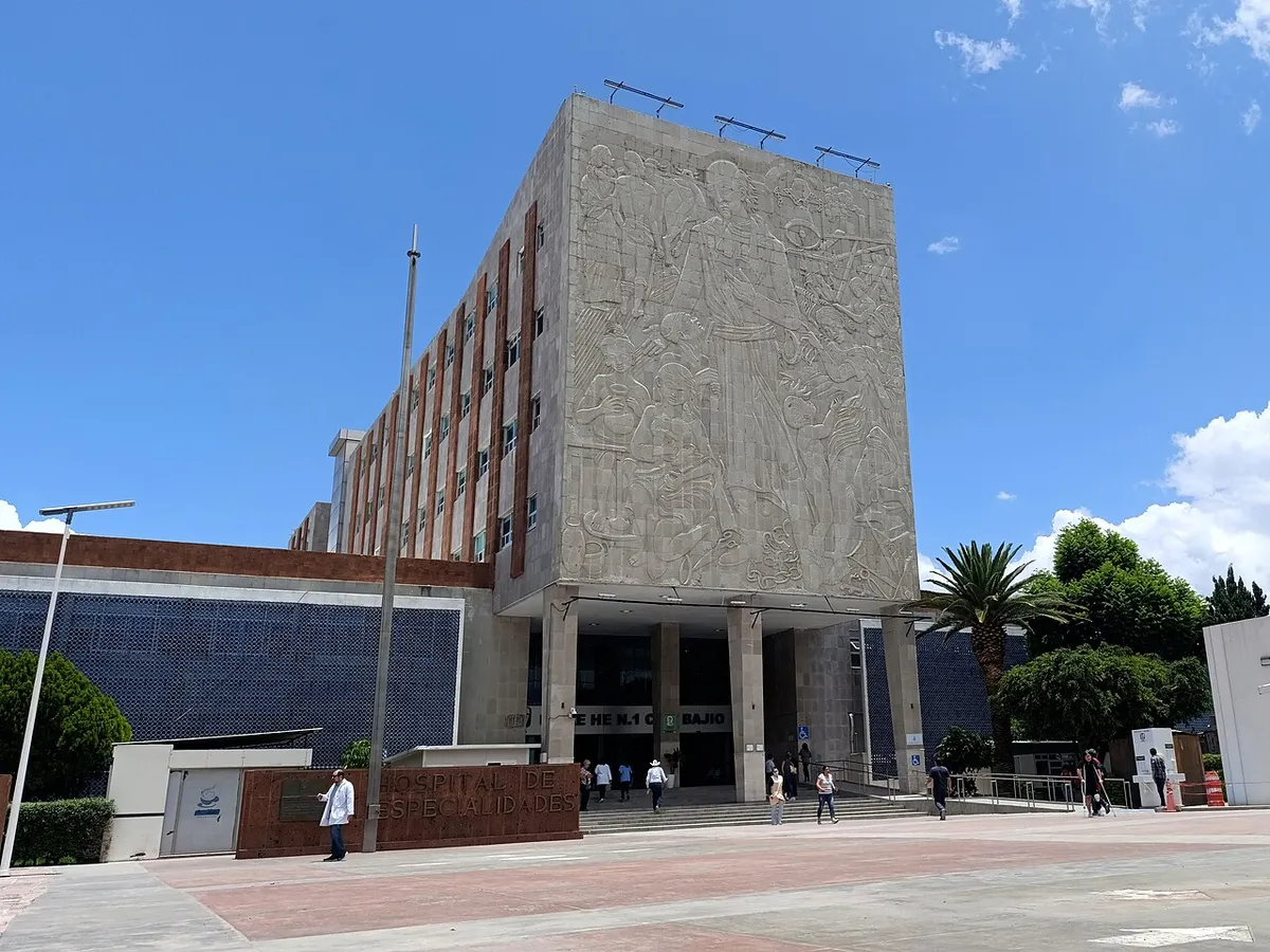 Fachada de un hospital con un mural monumental en su torre principal y explanada de acceso