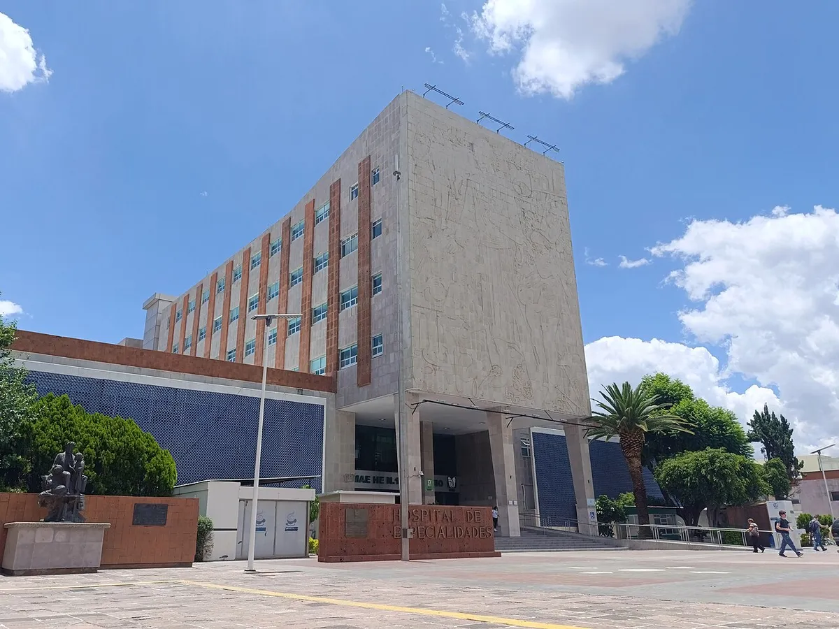 Vista lateral de un hospital del IMSS con su torre de consultorios y una explanada arbolada