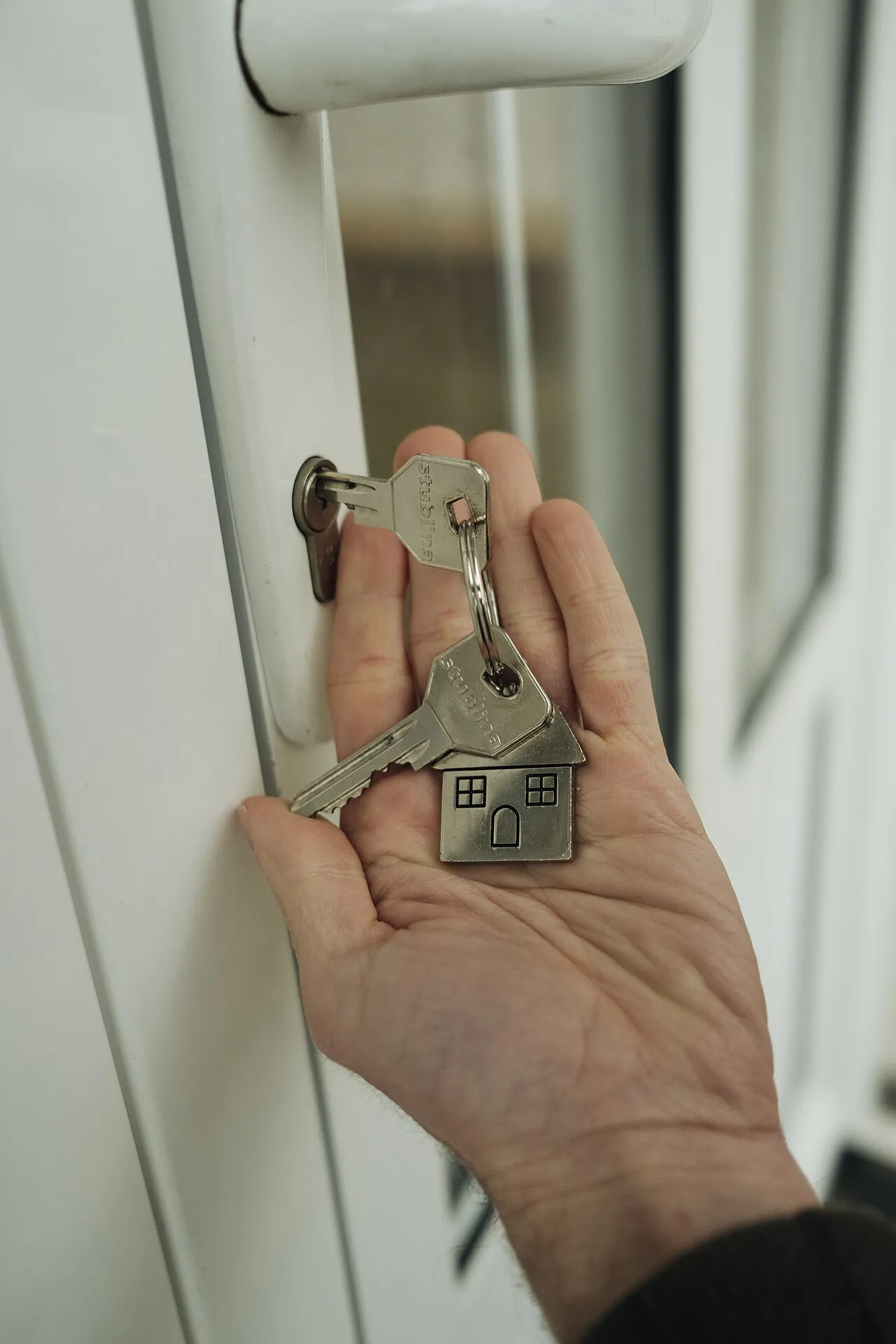 Una mano sostiene un llavero con forma de casa junto a la manija de una puerta