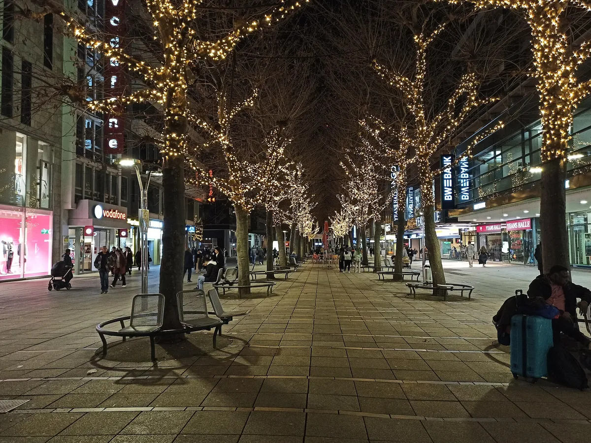 Rua de pedestres à noite com árvores enfeitadas com luzes de Natal douradas