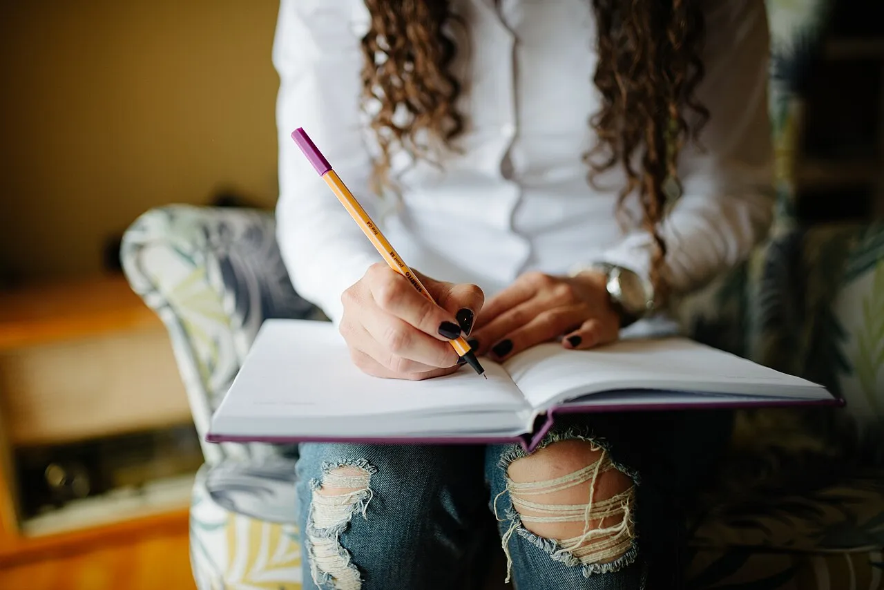 Manos de una mujer escribiendo con lápiz en una agenda abierta sobre sus piernas