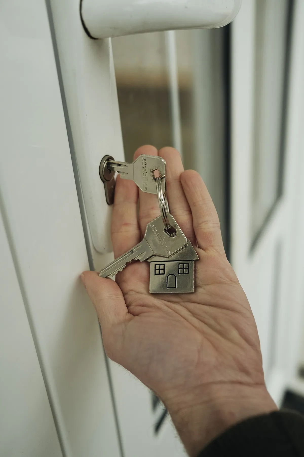Mão segurando as chaves de uma casa junto à fechadura da porta, no momento da entrega do imóvel financiado