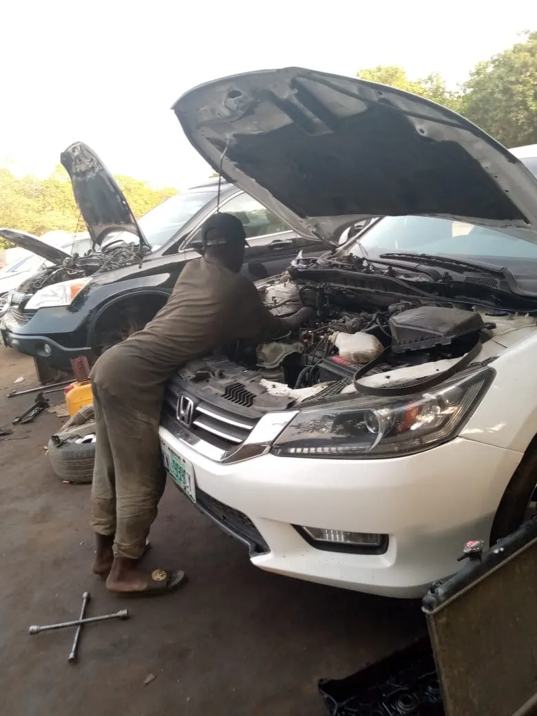 Un mecánico se inclina sobre el motor de un automóvil con el cofre abierto en un taller