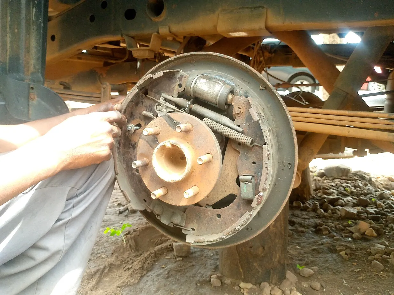 Manos de un mecánico trabajando en el tambor de freno de un automóvil elevado en un taller