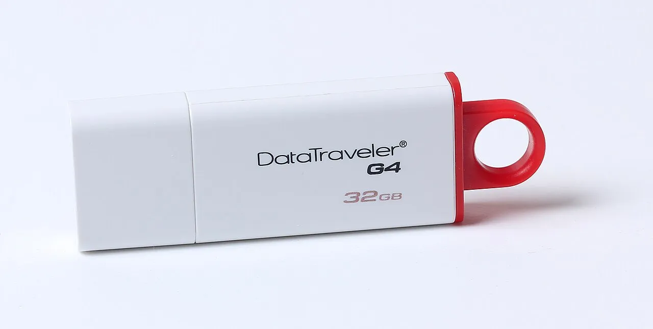 Una memoria USB blanca con detalle rojo apoyada sobre una superficie clara