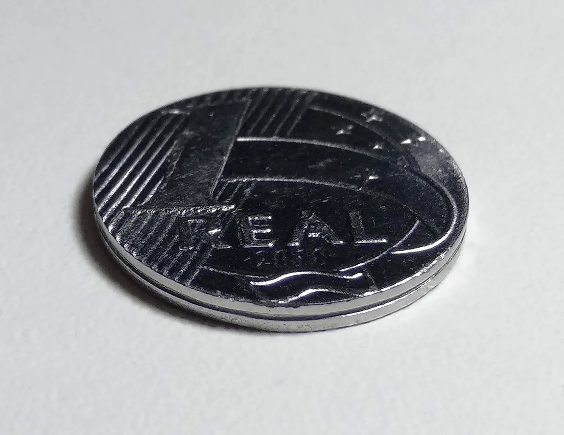 Detalhe ampliado de uma moeda de um real, representando os juros pagos mês a mês em um financiamento