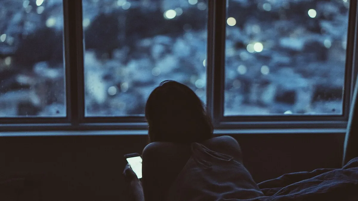 Mujer consultando su celular junto a una ventana por la noche