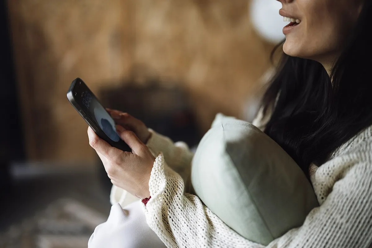 Mulher no sofá de casa usando o celular à noite