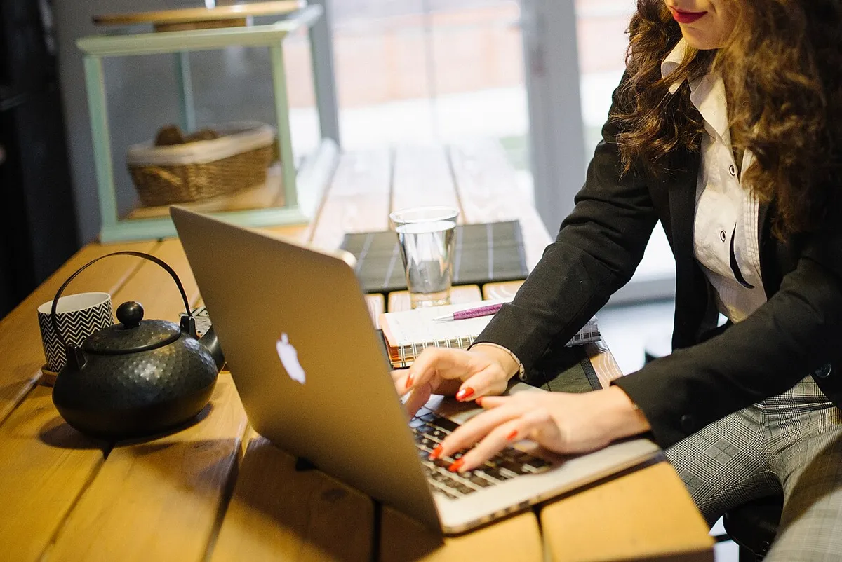 Mulher trabalhando em um laptop sobre uma mesa de madeira em casa, acessando serviços pelo computador