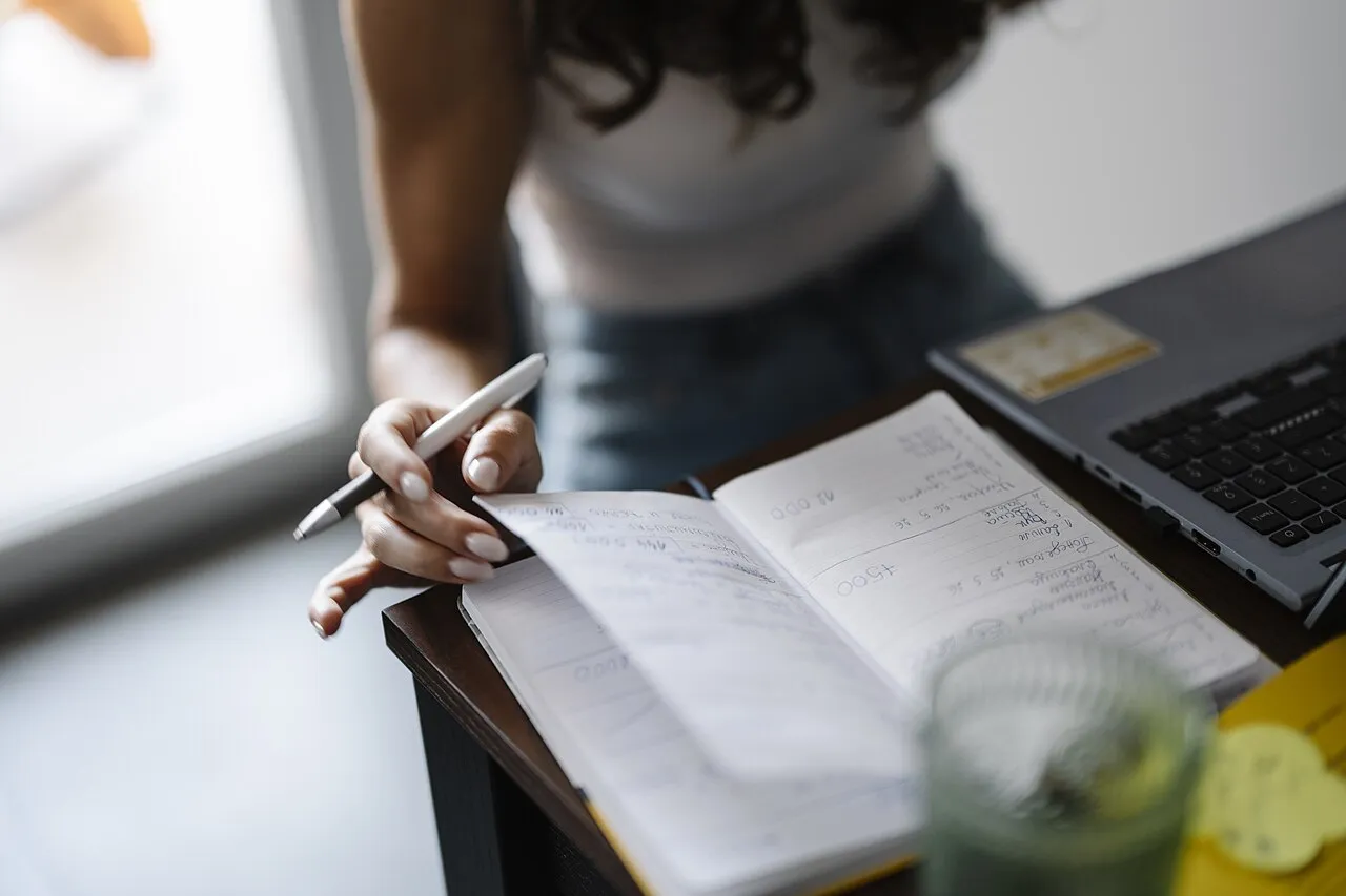 Una persona escribe en un cuaderno abierto junto a una laptop sobre un escritorio