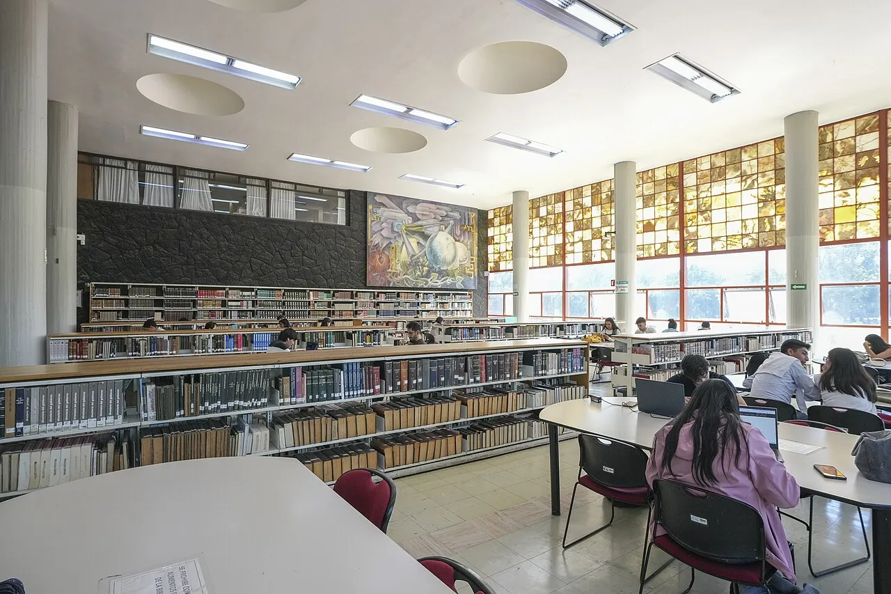 Sala de consulta de la Biblioteca Central de la UNAM con estudiantes estudiando entre estanterías