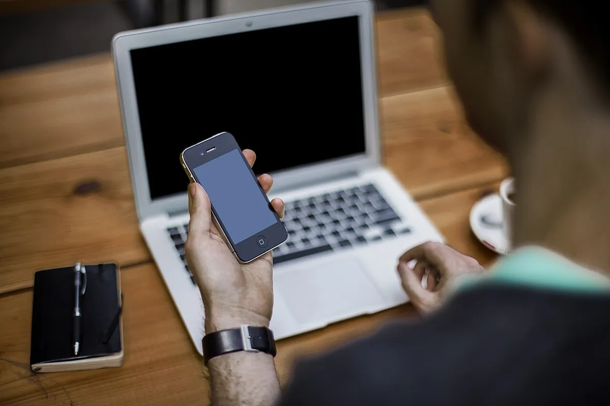Una persona trabaja en su registro en línea con el celular y la computadora portátil sobre la mesa